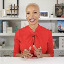 A woman sits at a table in the middle of speaking with a smile on her face.