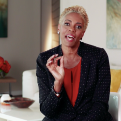 A woman sits on a couch speaking with her hand in motion.