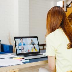 A light-skinned woman sits at a desk on a web call with colleagues.