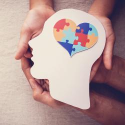 Hands hold a wooden cut out of a person's head with a heart shaped brain.