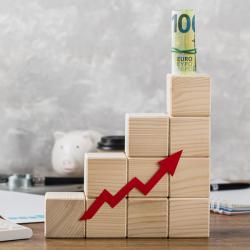 A stack of wooden blocks in the shape of a staircase with an arrow pointing up. Money sits on the top block.