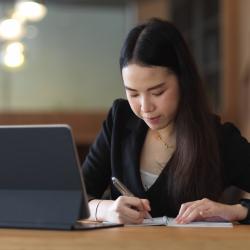 A woman takes notes with a laptop in front of her.