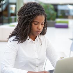 A dark skinned woman works at a computer. 