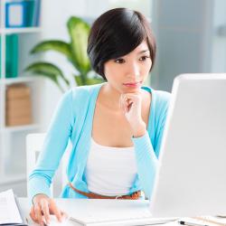 A medium-light skinned woman sits working at a computer.