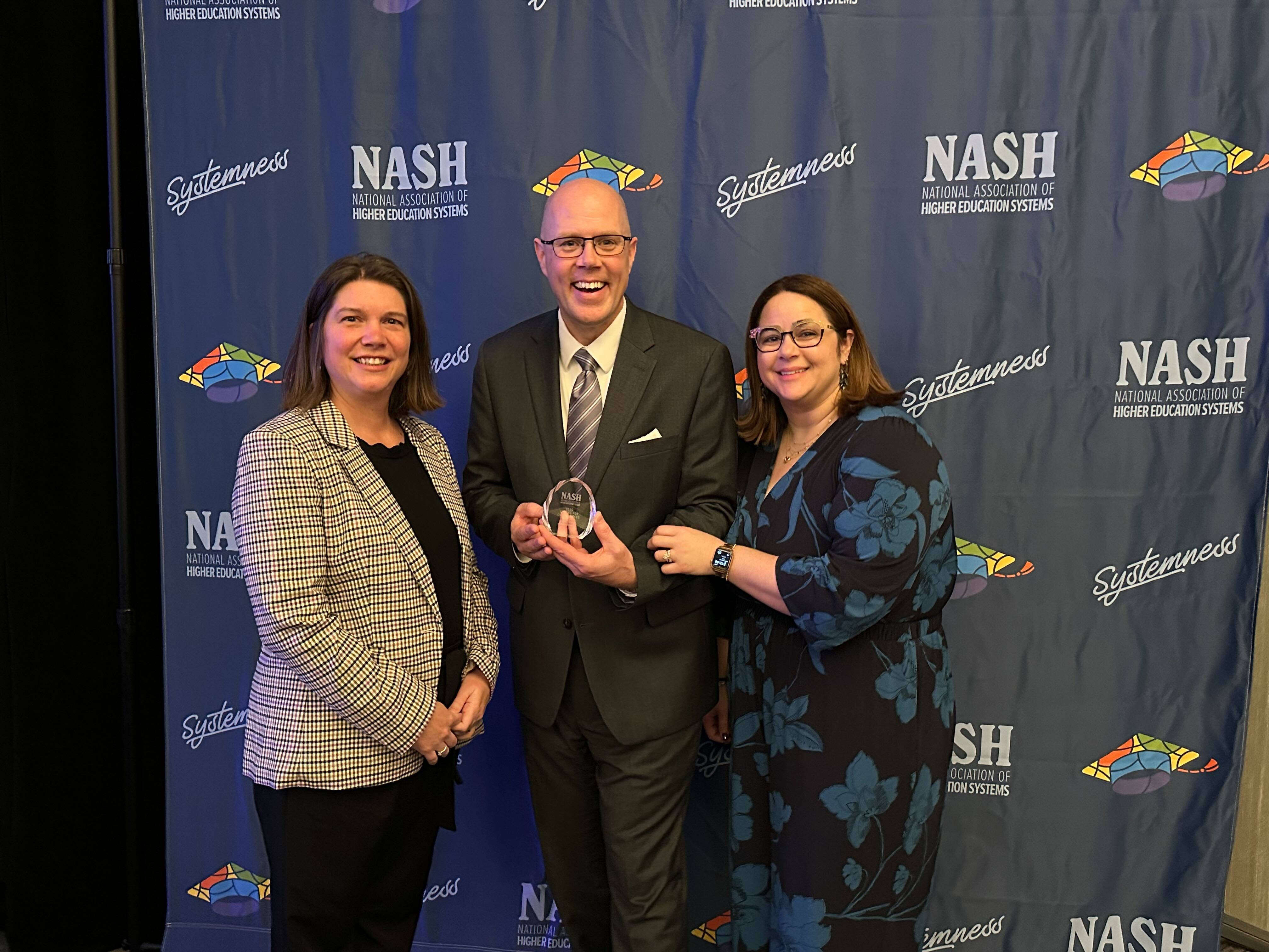 Three people, Associate Vice President LeeAnn Pasquini (left) Chief Procurement Officer Michael Durkin (center) and and NASH Interim President Jessica Todtman (right) posing in front of a navy background with NASH logo