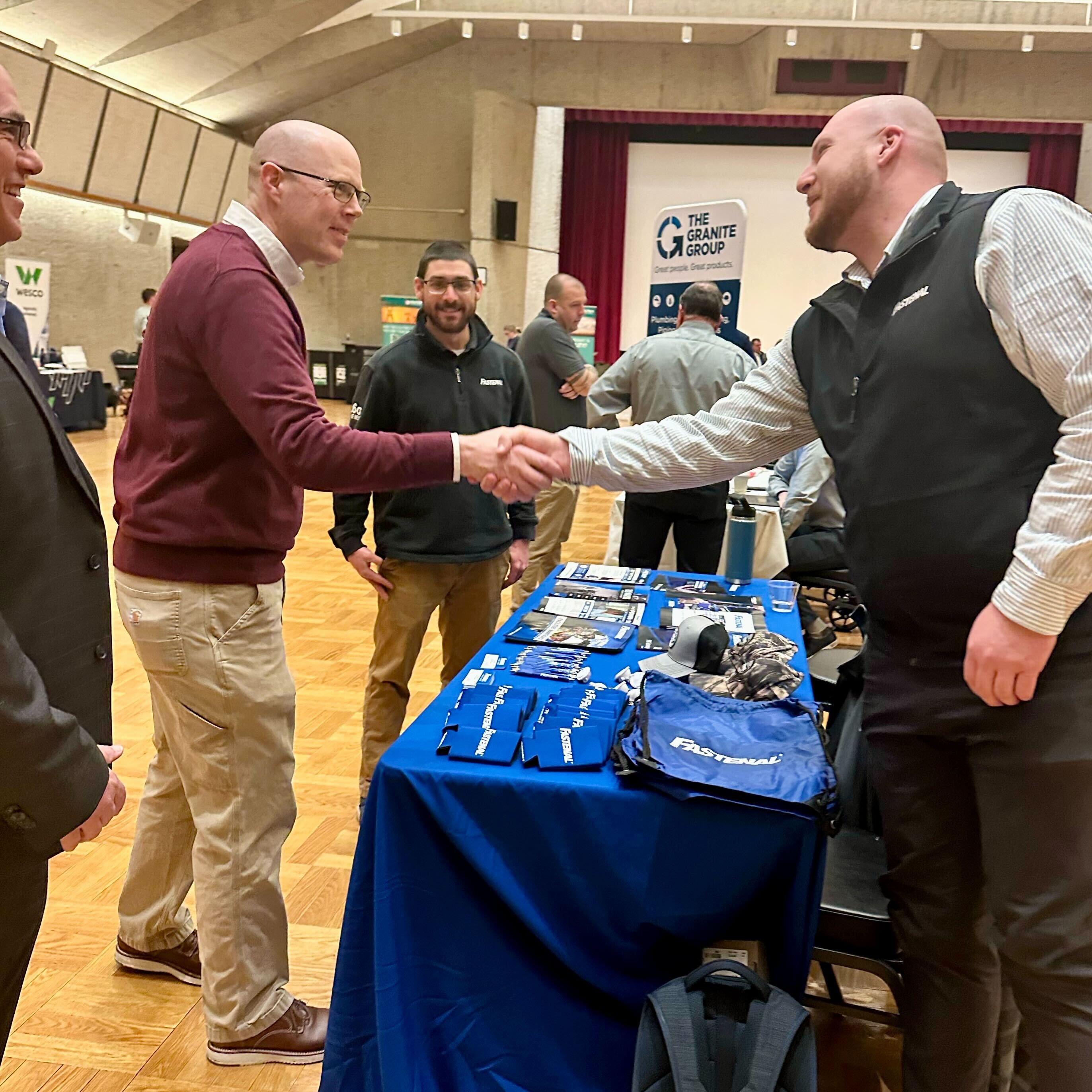 Two people shaking hands over a table covered with a blue tablecloth